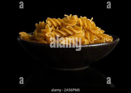 Beaucoup d'aliments complets secs fusilli dans dark brown Bol en céramique isolé sur verre noir Banque D'Images