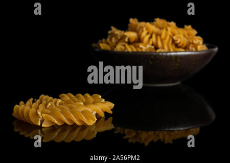 Beaucoup d'aliments complets secs fusilli dans dark brown Bol en céramique isolé sur verre noir Banque D'Images