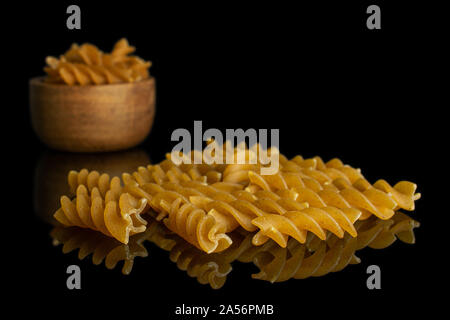 Beaucoup d'ensemble brun sec de farine les fusilli grand groupe est à l'avant et le reste est dans le petit bol en bois isolé sur verre noir Banque D'Images