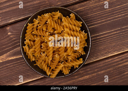 Beaucoup d'aliments complets secs fusilli dans dark brown Bol en céramique flatlay sur bois marron foncé Banque D'Images