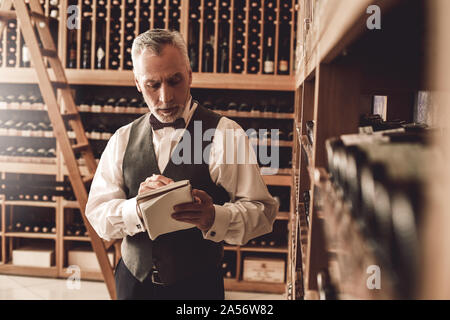 Sommelier Concept. Man en prenant des notes sur la variété de vins concentrés d'ordinateur portable Banque D'Images