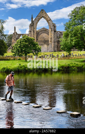 L'homme de traverser la rivière Wharfe sur les pas japonais au 12e siècle, église du prieuré augustinien Bolton Bolton Abbey ruines cimetière avec l'Angleterre Banque D'Images