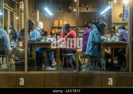 Les clients travailler et profiter de la connexion Wi-Fi gratuite dans un café à Chelsea à New York le mardi, Octobre 8, 2019. Le wi-fi et les tables communes encouragent l'utilisation de la cafétéria comme un espace de co-working. (© Richard B. Levine) Banque D'Images