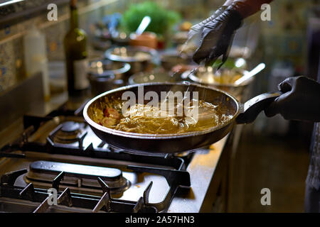 Concept alimentaire. Le chef se mélange rapidement spaghetti dans une casserole les tomates et les huîtres, les mains se déplacent et flou. Le processus de cuisson de spaghettis aux fruits de mer. Banque D'Images
