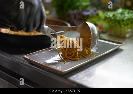 Concept alimentaire. Le chef mélange spaghetti dans une casserole les tomates et les huîtres, le plat dans un restaurant. Le processus de cuisson de spaghettis aux fruits de mer. Banque D'Images