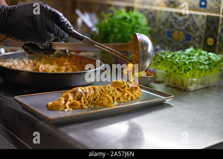 Concept alimentaire. Le chef mélange spaghetti dans une casserole les tomates et les huîtres, le plat dans un restaurant. Le processus de cuisson de spaghettis aux fruits de mer. Banque D'Images