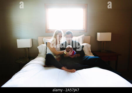 Deux nouveaux parents sourire à leur fils nouveau-né alors qu'il était assis sur un lit Banque D'Images