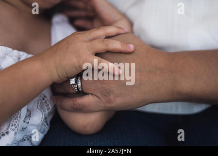 L'enfant main posée sur la main de la mère portant des anneaux de mariage Banque D'Images