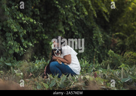 Femme en blanc shirt hugging animal Chien tricolore dans un écrin de verdure Banque D'Images