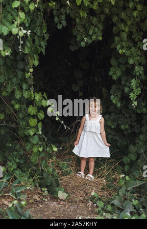 Souriante jeune fille en robe blanche sous le couvert de plantes vining Banque D'Images