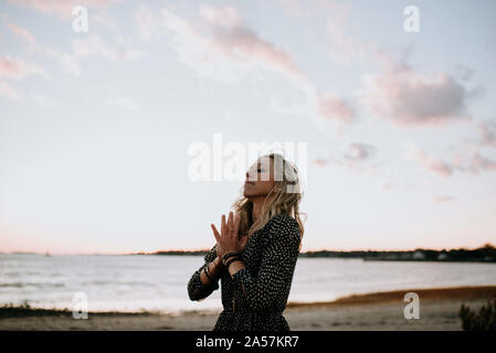 Femme méditant sur la plage au coucher du soleil Banque D'Images