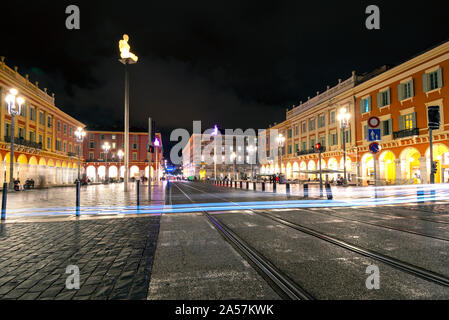 Les phares de voitures faire la lumière sentier à partir de l'exposition longue comme la croix de tramway tard dans la nuit à la Place Massena dans la ville historique de Nice, France. Banque D'Images