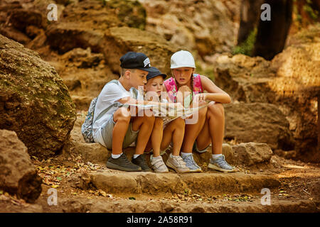 Garçon et fille avec deux sacs à dos, assis sur les marches à proximité de rochers et de la lecture site ensemble lors d'un voyage Banque D'Images