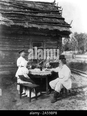 Genre scène vue inclut l'homme avec de la balalaïka, samovar sur la table, verser à boire, l'homme garçon par fenêtre et d'autres assis à table à l'extérieur d'une maison au toit de chaume. S paysan russe 1875 Banque D'Images