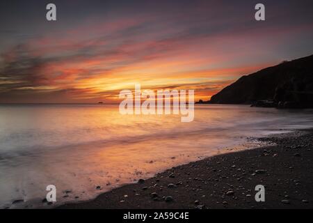 Coucher de soleil à couper le souffle sur l'océan calme à Polkerris, Cornouailles, Royaume-Uni Banque D'Images