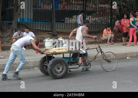 Deux hommes en blanc T-shirts pousser leur vélo de transport à trois roues d'une colline dans le centre de La Havane. Banque D'Images