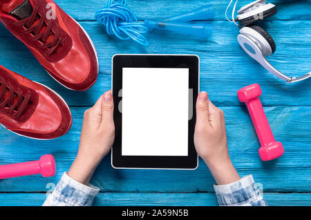 Ordinateur tablette avec écran noir main de femme en rouge, sneakers, la corde à sauter, haltères et un casque bleu sur fond de bois. Banque D'Images