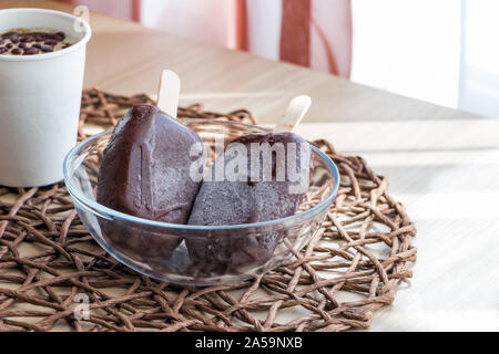 Végétalien premières glaces faites maison, fait à partir de la banane et la crème de coco, couverts de chocolat naturel. Petite partie dans du papier blanc tasse et deux sucettes glacées Banque D'Images