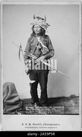 Peu d'Oglala, leader du groupe, portrait studio, debout, face à l'avant, portant une coiffe de l'avertisseur sonore, pantalon et chemise, et la tenue d'arc, de flèches et de tomahawk. Banque D'Images