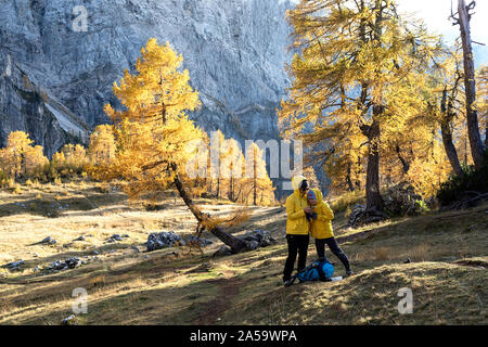 La mère et le fils debout sur le plateau couvert de graminées dans les montagnes, looking at smartphone, pins colorés en automne. Alpes Juliennes , Slovénie Banque D'Images