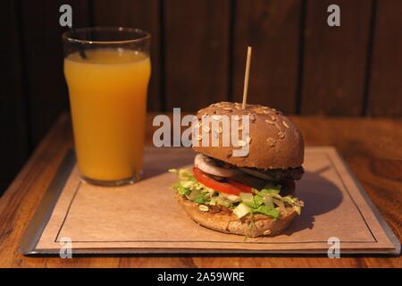 Gros plan du home made burger americano sur fond de bois avec verre de jus d'orange Banque D'Images