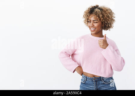 Hé, vous êtes meilleur. Portrait de Christian et charismatique heureux african american woman avec coupe de blonde avec un clin d'joyeusement et sourire comme showing thumb up Banque D'Images