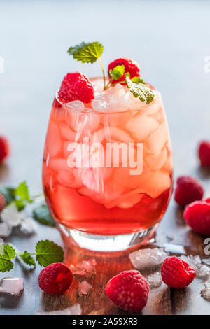 Close-up of a une rafraîchissante boisson translucide rouge avec de la glace et les framboises. Le jus est garnie d'une feuille verte, et therer sont des morceaux de glace et Banque D'Images