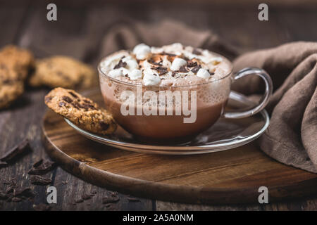 Chocolat chaud avec de la crème fouettée dans une tasse en verre sur une soucoupe en verre. Le chocolat est saupoudré avec un peu de chocolat noir râpé. Il y a quelques chocola Banque D'Images