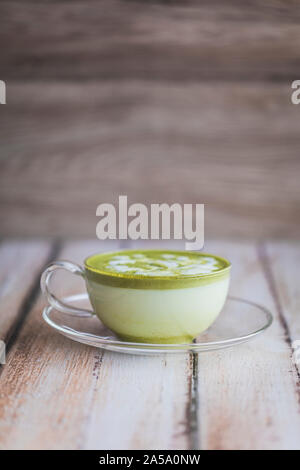 Thé vert matcha latte sur une table en bois. Le thé est la boisson mousseuse en bonne santé dans une tasse en verre avec une soucoupe, sur une table en bois. La photo a une bonne montant o Banque D'Images