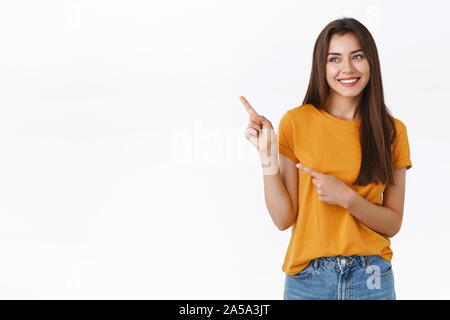 Gai, insouciant heureux jeune femme sympathique au t-shirt jaune, souriant joyeusement de rire comme à l'angle supérieur gauche, enthousiaste avec pointage Banque D'Images