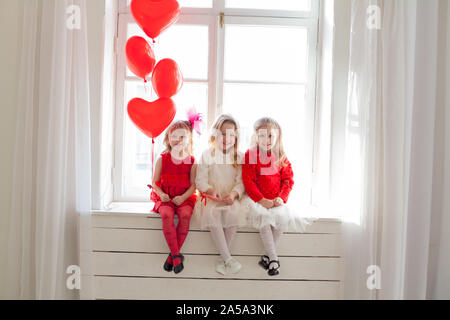 Trois petites filles s'assoient près de la fenêtre avec des ballons Banque D'Images