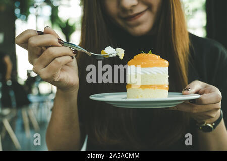 Image Gros plan femme asiatique d'une belle tenue et de manger un gâteau d'orange dans le café moderne Banque D'Images