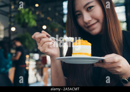 Image Gros plan femme asiatique d'une belle tenue et de manger un gâteau d'orange dans le café moderne Banque D'Images