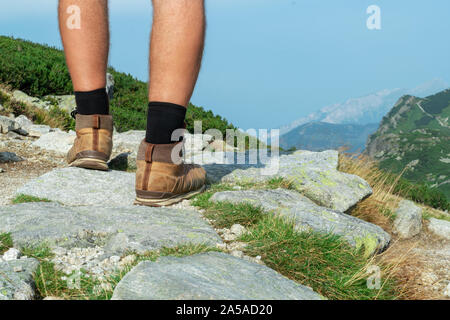 Les jambes d'un touriste en chaussures de randonnée gros plan sur un rocher sur un fond de montagnes, vue arrière Banque D'Images