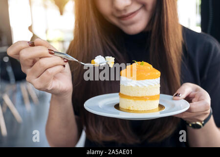 Image Gros plan femme asiatique d'une belle tenue et de manger un gâteau d'orange dans le café moderne Banque D'Images