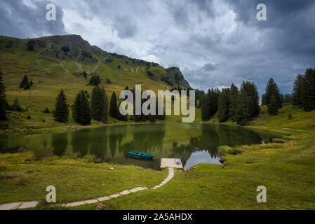 Lac de montagne avec un homme allongé sur le dos sur une jetée avec un bateau à rames Banque D'Images