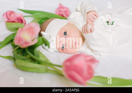 Un peu de nouveau-né belle jeune fille en robe blanche est étendue sur le lit au milieu des fleurs Banque D'Images