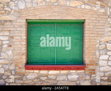 Fenêtre avec des volets verts et un rebord de rouge dans un vieux mur de pierre d'une maison Banque D'Images