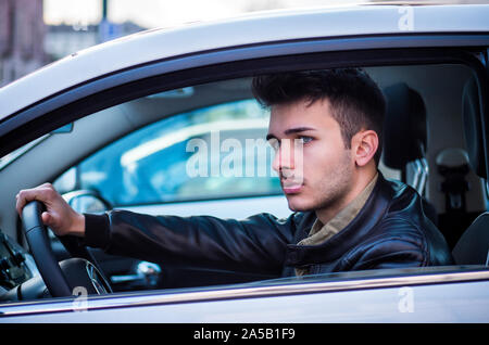 Beau jeune homme aux yeux bleus assis dans sa voiture Banque D'Images