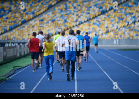 Groupe de personnes d'exécution sur les voies du stade dans la lumière du soir Banque D'Images