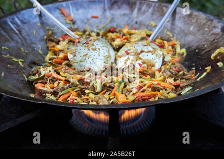 Délicieux petit wok est cuit dans une grande poêle sur une cuisinière à gaz. Banque D'Images