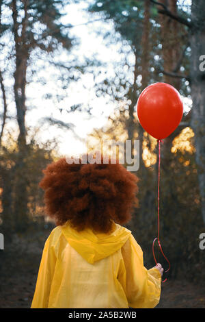 Femme dans un imperméable jaune tenant un ballon rouge sur l'arrière-plan de forêt. Femme marche dans les bois dans un ciré, attendant la pluie. Banque D'Images