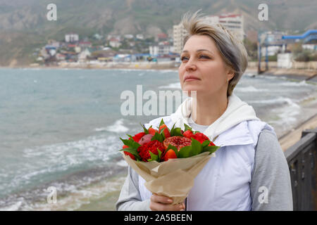 Belle jeune femme se tient sur le bord de la mer avec un bouquet dans ses mains Banque D'Images