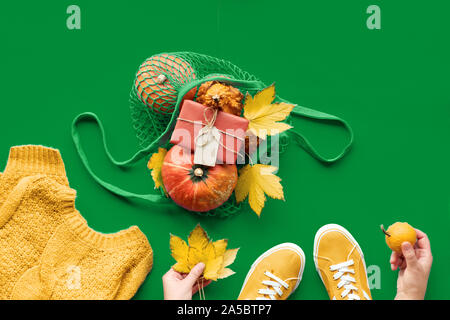 Mise à plat d'automne jaune saffran et jig irlandaise de vert, couleur à la mode pour l'automne 2021. Citrouilles Orange en sac-filet, feuilles d'érable, les mains en w Banque D'Images