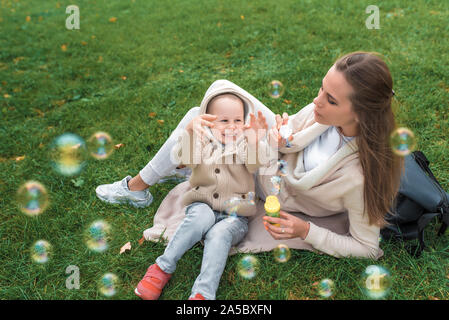 Femme maman avec un petit garçon fils de 4-5 ans, se coucher sur l'herbe. Les bulles de savon sont lancées. Les gens heureux jouer rire et s'amuser des émotions positives Banque D'Images