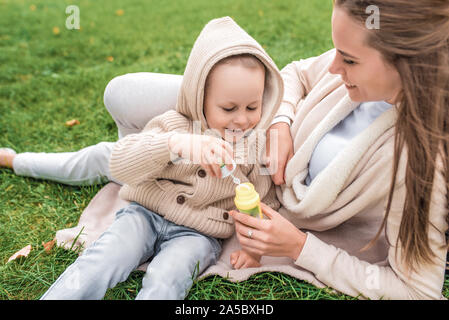 Les bulles de savon sont lancées. Femme maman avec un petit garçon fils de 4-5 ans, se coucher sur l'herbe. Les gens heureux jouer rire et s'amuser des émotions positives Banque D'Images