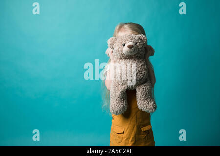 Fille sur un fond bleu serrant un ours gris. Elle est très heureuse Banque D'Images