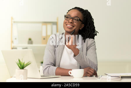 Afro Businesswoman Sitting At Laptop imaginer quelque chose dans Office Banque D'Images