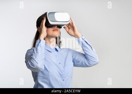 Jeune femme au casque de réalité virtuelle debout sur fond gris Banque D'Images