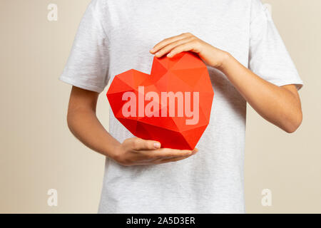 Boy holding polygonale 3d papier rouge coeur dans ses mains Banque D'Images